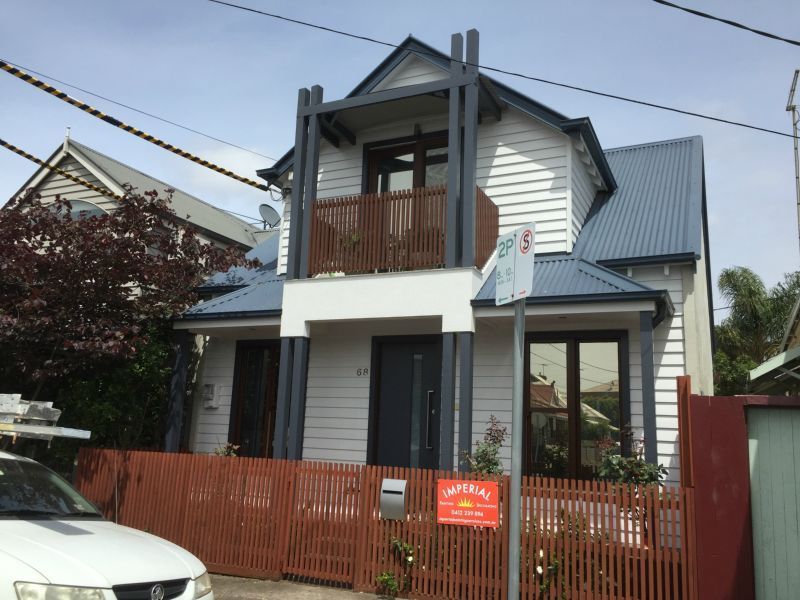 Two-story white house with dark gray trim, a balcony, and a red fence. A car is parked in front.