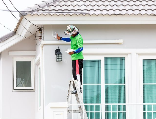 A man is standing on a ladder painting a house.