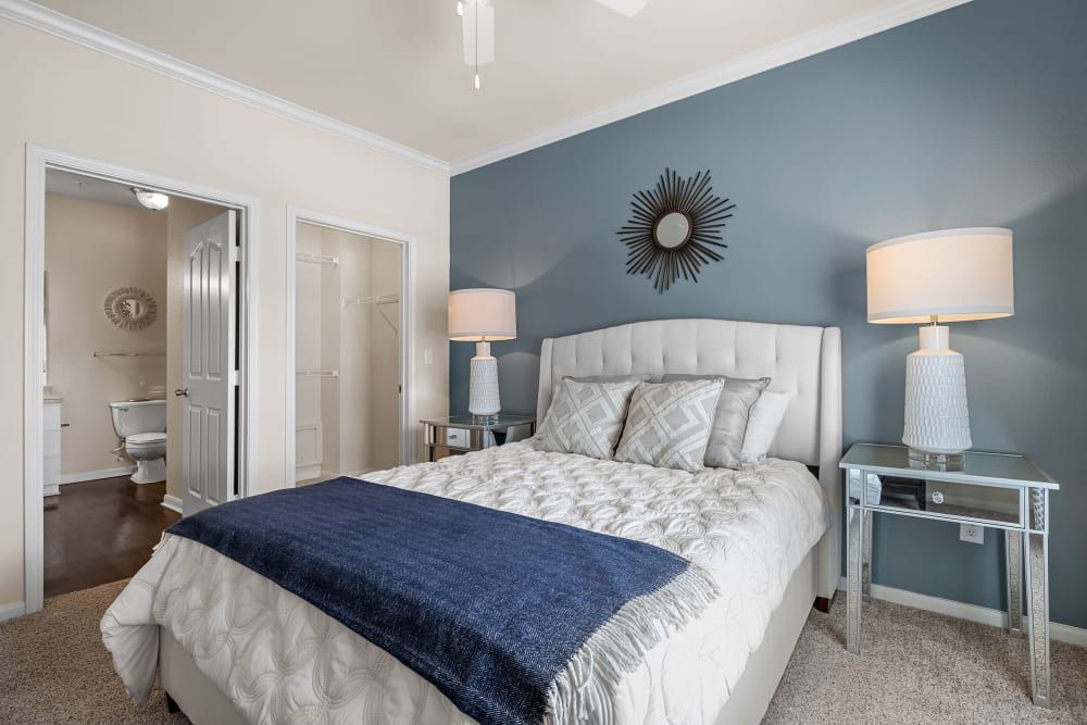 Modern bedroom with a bed, nightstand, lamps, and a blue wall at Marquis at The RIM in Northwest San Antonio, TX.