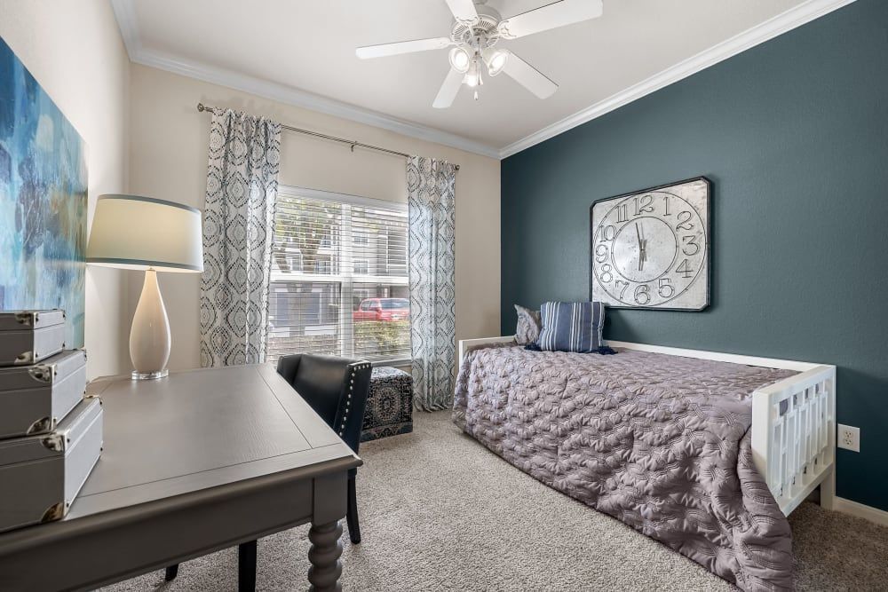 A bedroom with a bed, desk, lamp, and ceiling fan at Marquis at The RIM in Northwest San Antonio, TX.