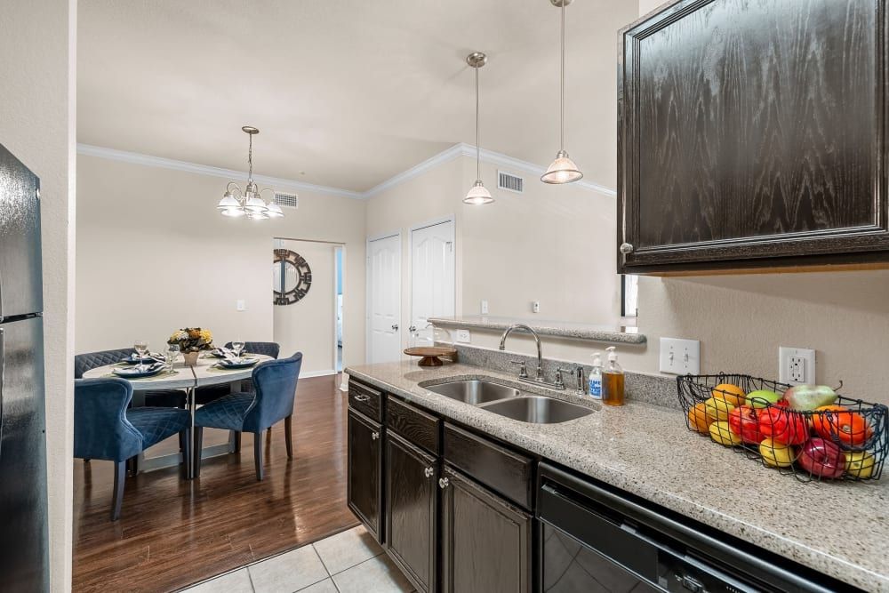 Apartment kitchen with a sink, dishwasher, refrigerator, and dining room in the background at Marquis at The RIM in Northwest San Antonio, TX.