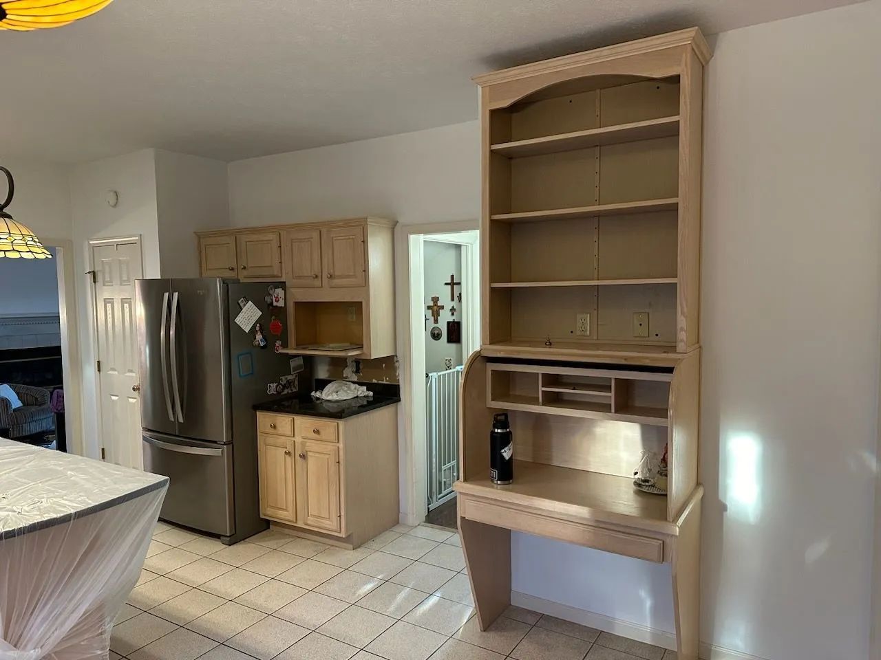 Kitchen with stainless steel fridge, wood cabinets, tiled floor, and a built-in shelf unit by the wall