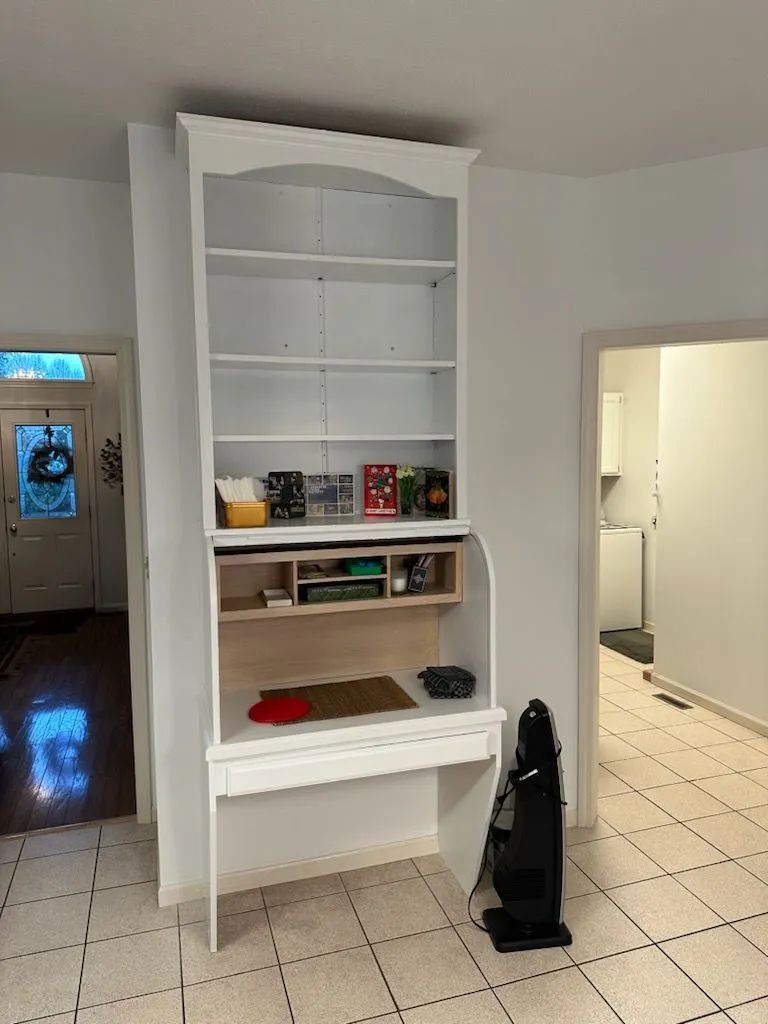 White built-in shelving in a tiled hallway, with a black vacuum beside an open doorway.