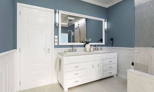 Modern bathroom with blue walls, white vanity, large mirror, and tiled tub area