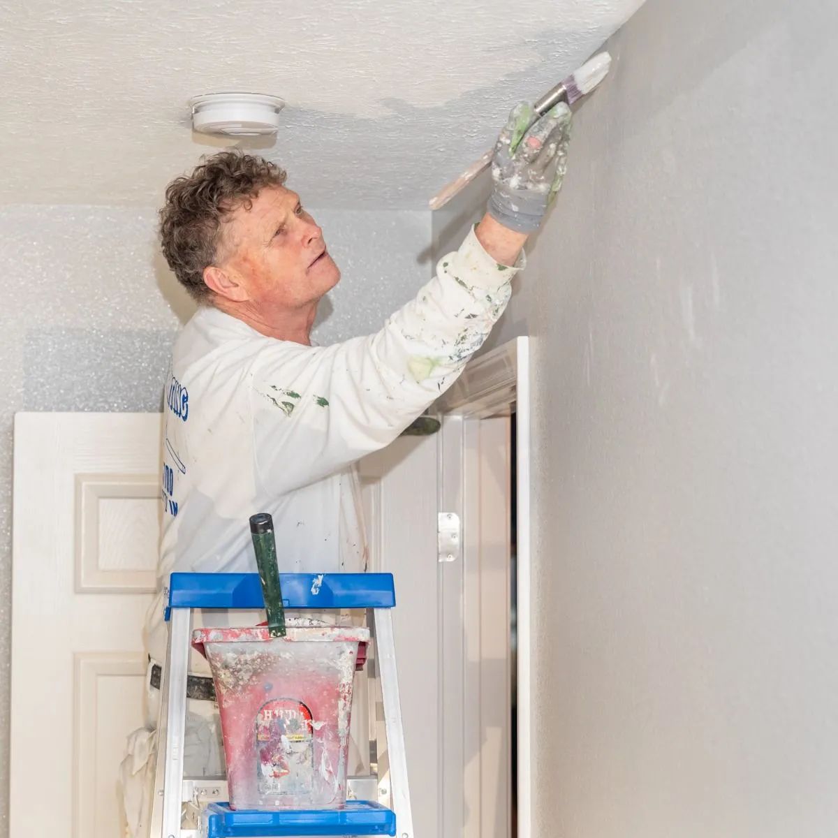 Painter using a roller to paint a ceiling in a room, standing on a ladder