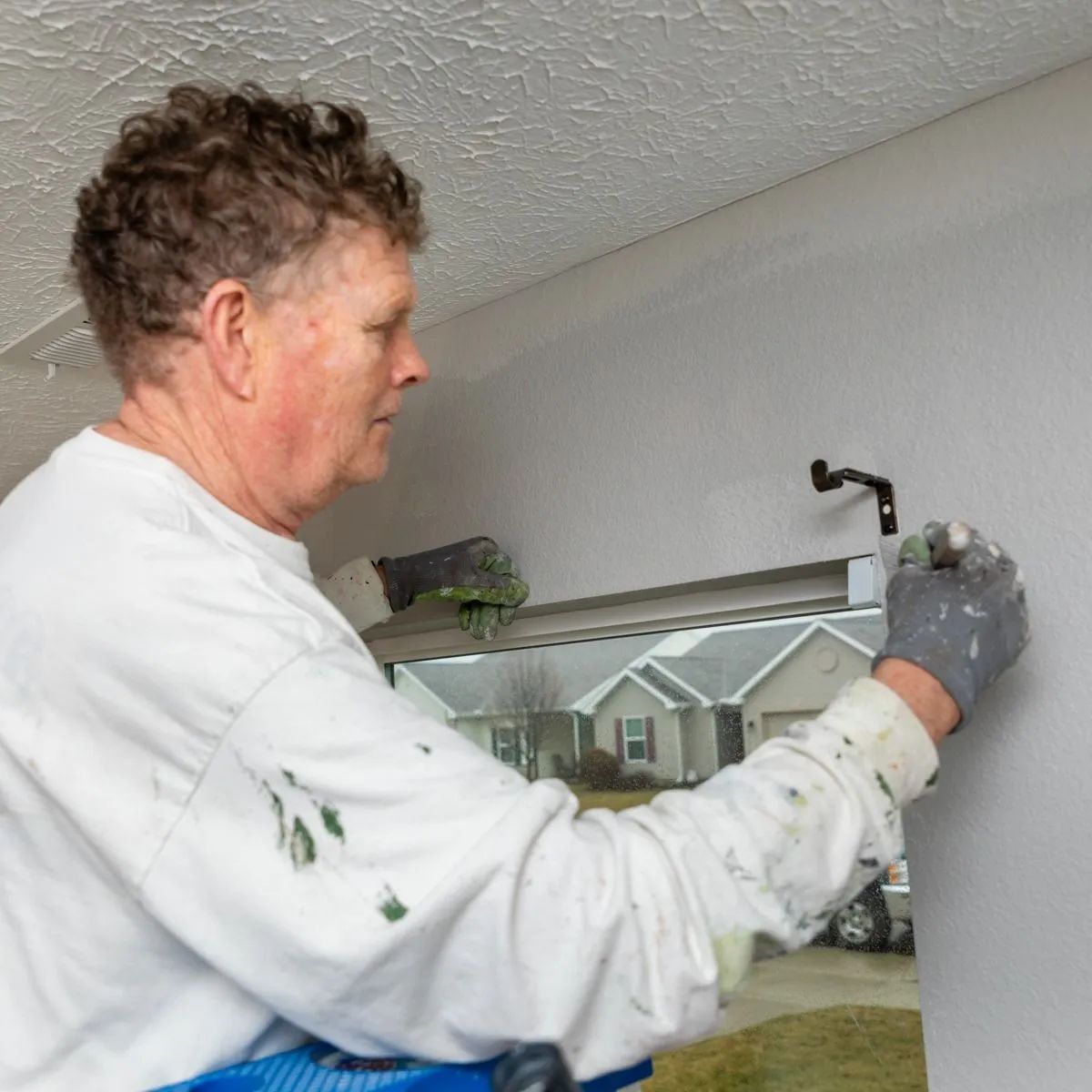 Person painting an interior wall with a roller near a window