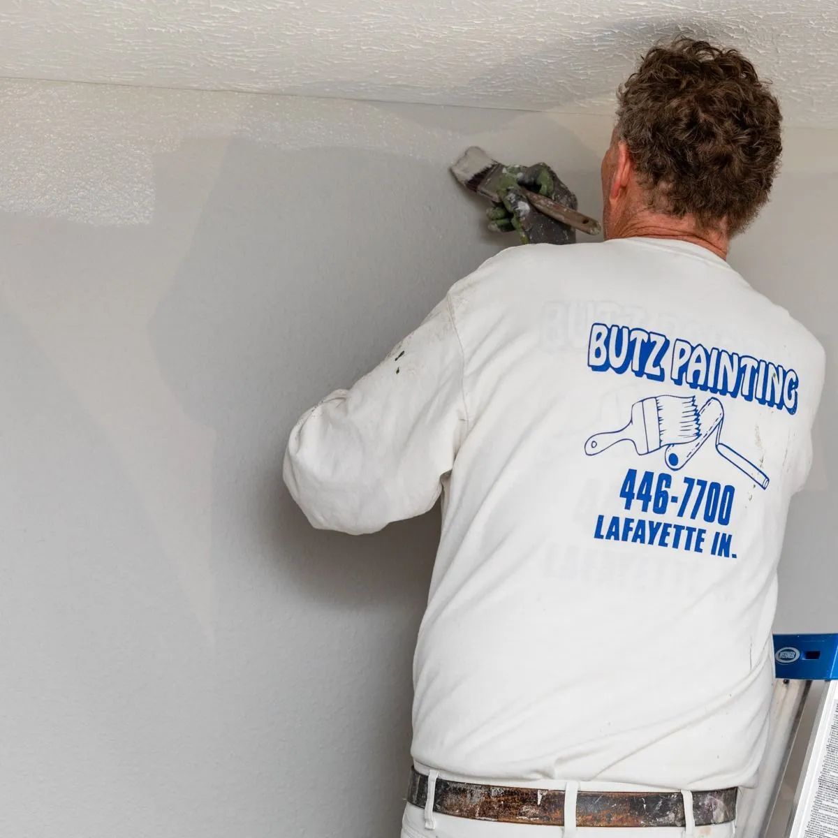 Painter in white shirt applying paint to a light gray wall with a spray gun.