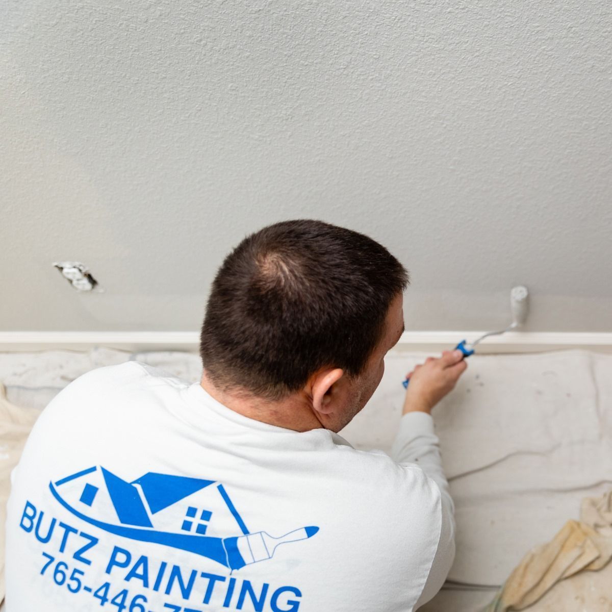 Painter in a white shirt with a blue logo paints a wall edge with a small brush.