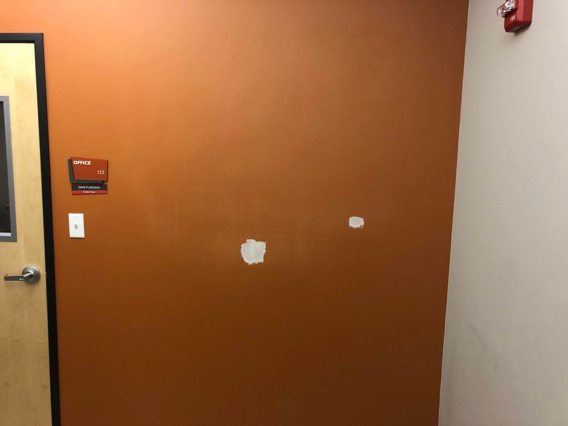 Orange hallway wall with two white patches and a door handle on the left