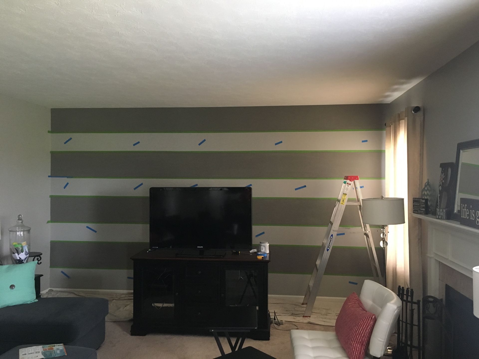 Living room with striped accent wall, TV stand, ladder by the window, and fireplace on the right