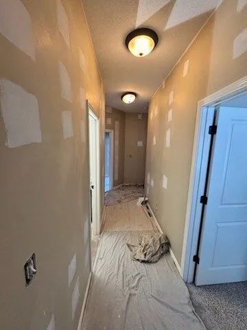 Narrow hallway under renovation with drywall patches, covered floor, and ceiling lights.