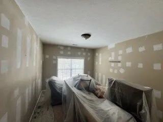 Living room under renovation, with plastic-covered furniture and patchy beige walls.