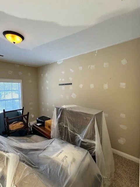Bedroom under renovation with plastic-covered furniture and beige walls marked for painting.