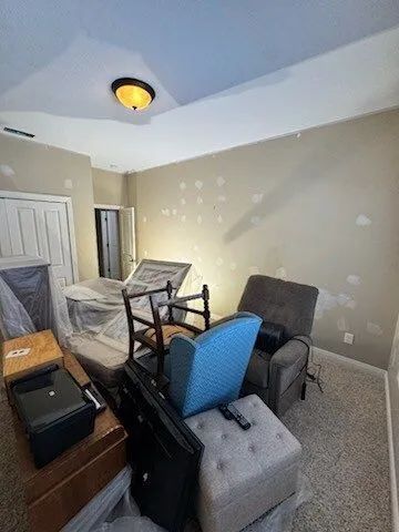Cluttered bedroom with stacked furniture and boxes, beige walls, and a ceiling light.