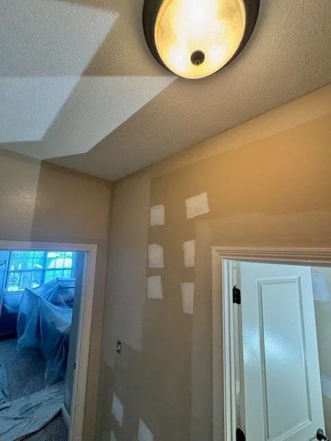 Small hallway with beige walls, ceiling light, paint patch tests, and an open doorway to a blue-lit room.