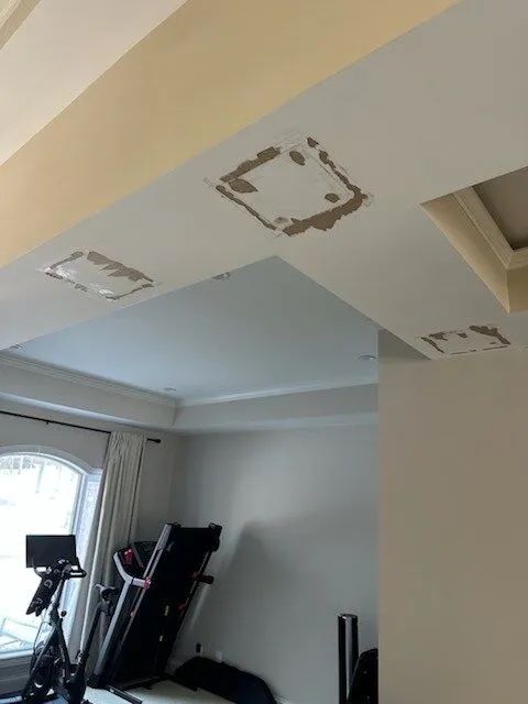 Ceiling with three damaged or patched light fixture areas in a room with exercise equipment near a window