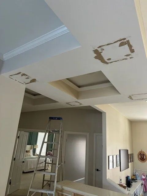 Ceiling with water-damage patches and a ladder in a home interior during repair работы