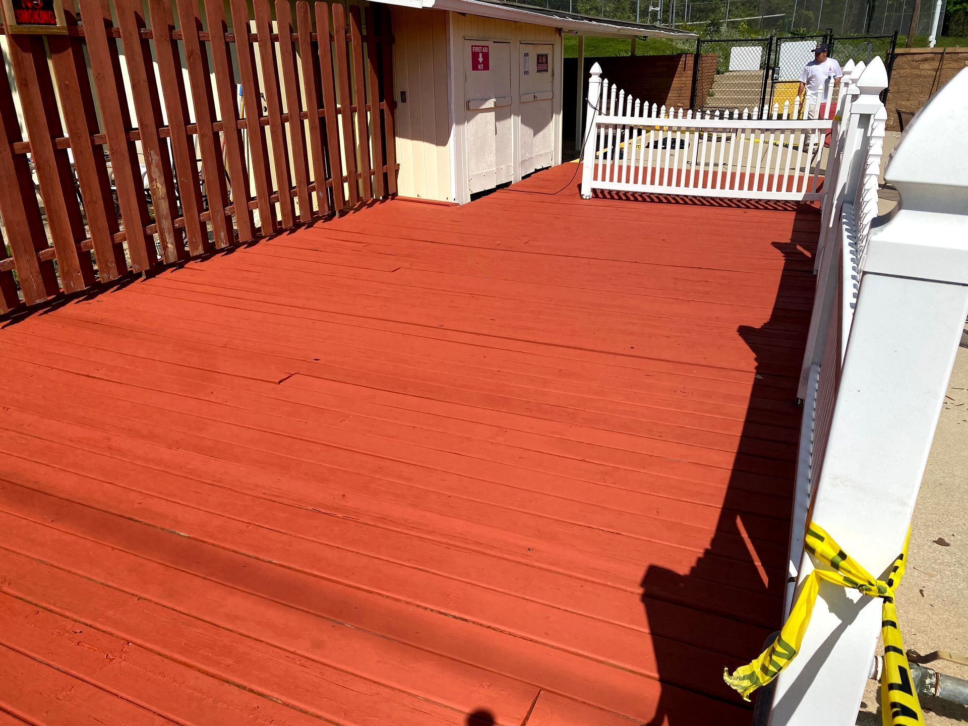 Red painted wooden deck with a white gate and fence, bordered by brown slats and a caution tape on the right