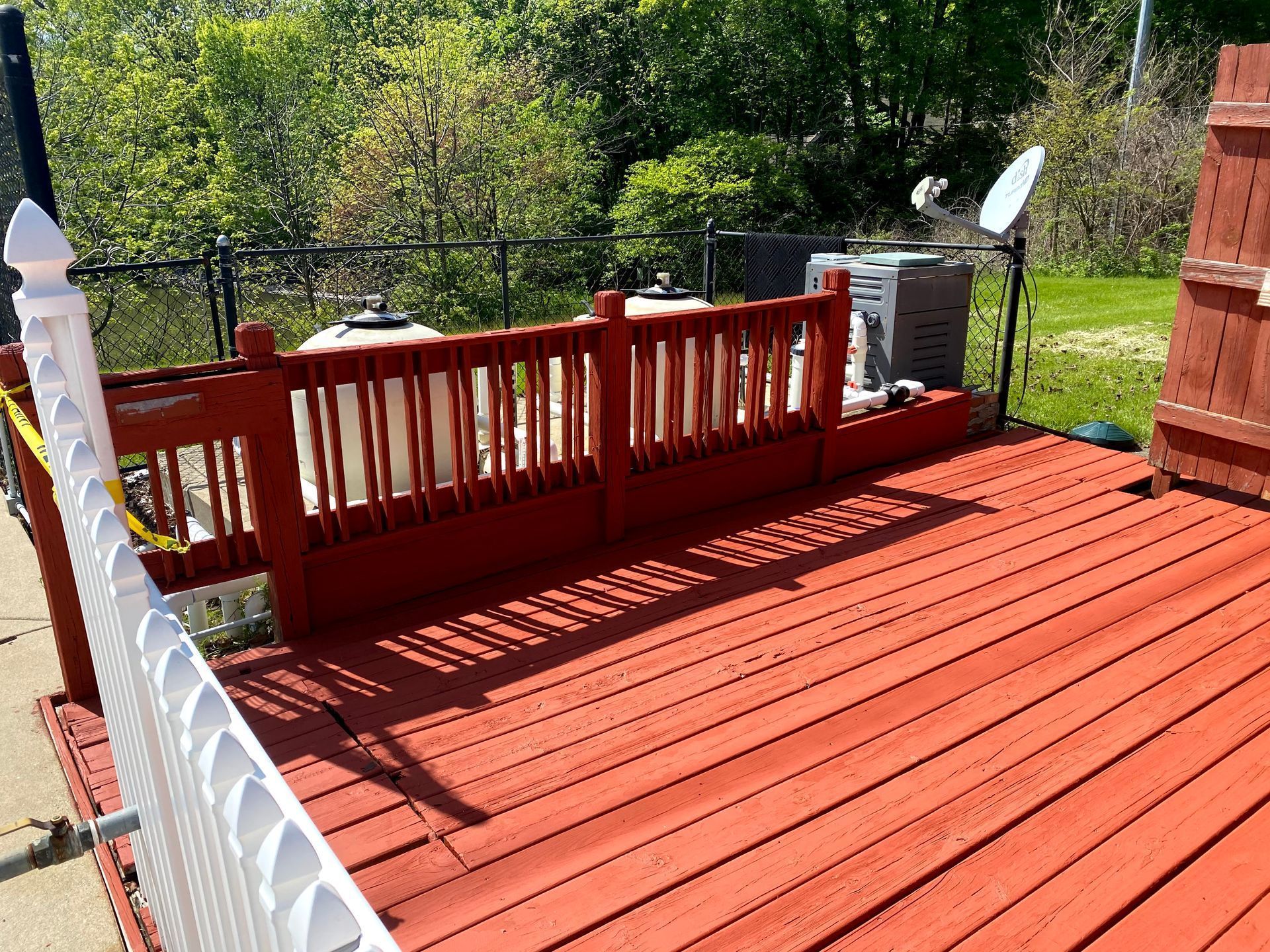 Red wooden deck with railing and stairs, overlooking trees in a sunny backyard
