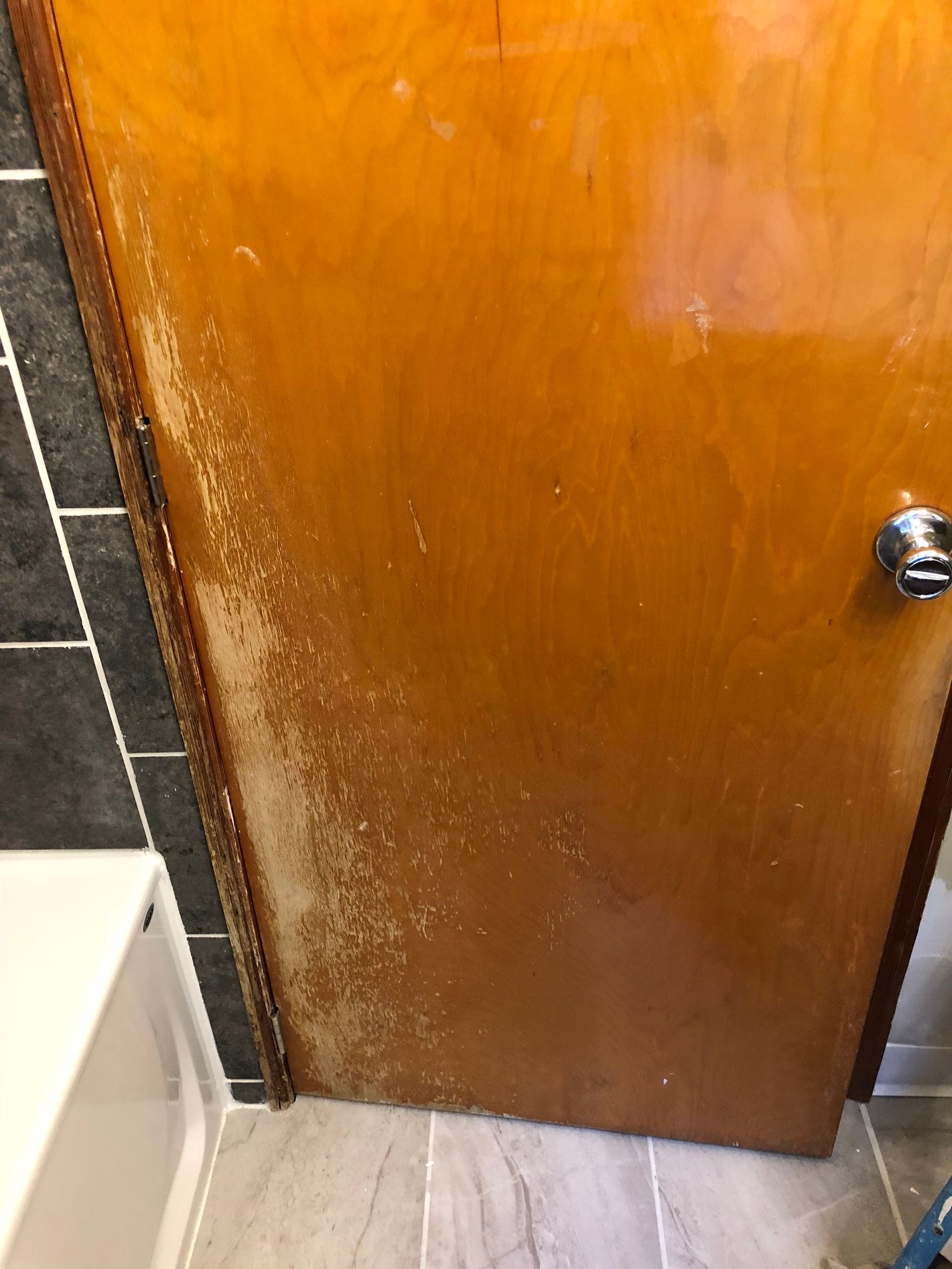 Partially open wooden bathroom door beside a white sink and dark tiled wall