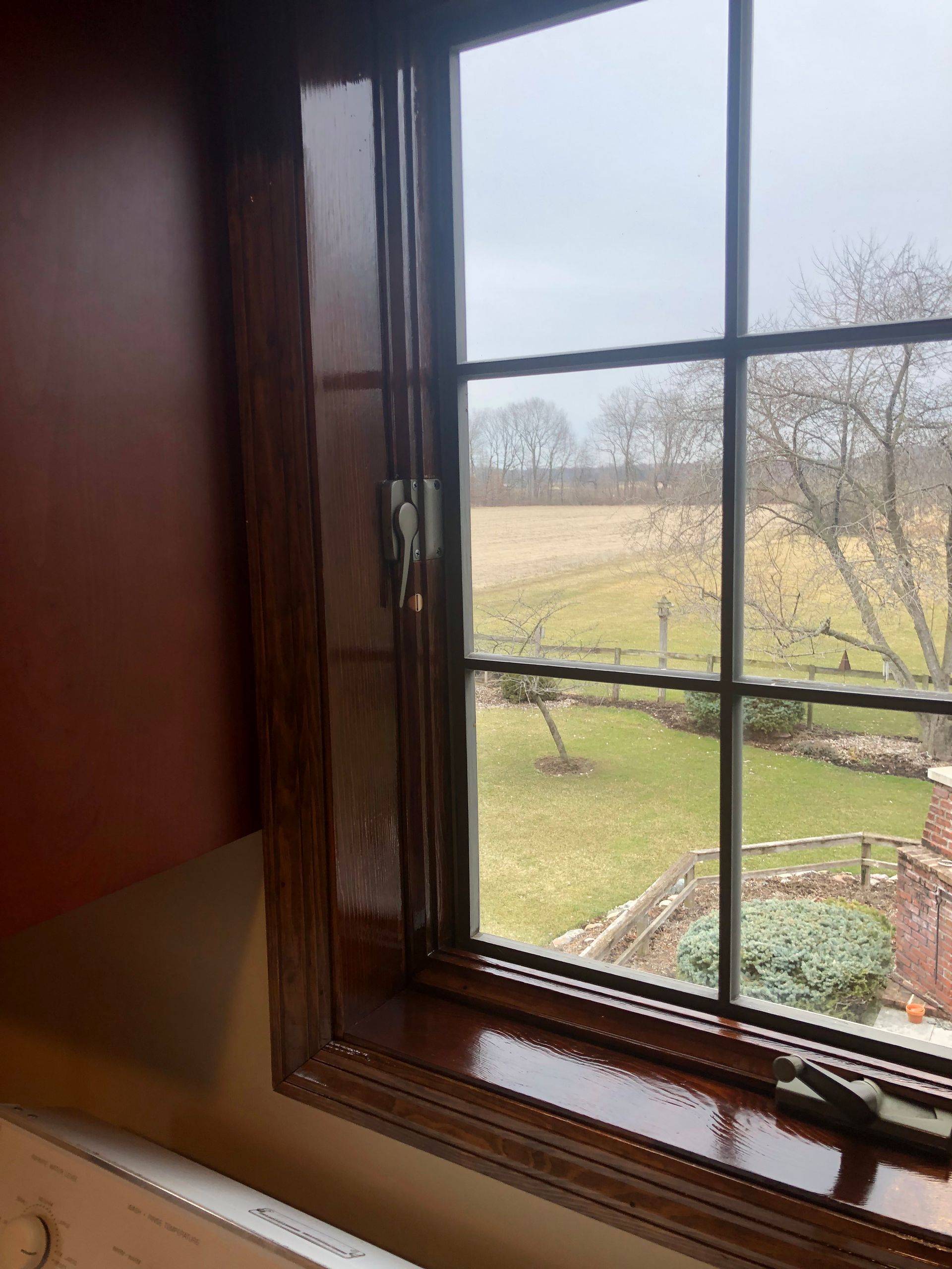 Wooden window looking out onto a grassy field and leafless trees on a cloudy day