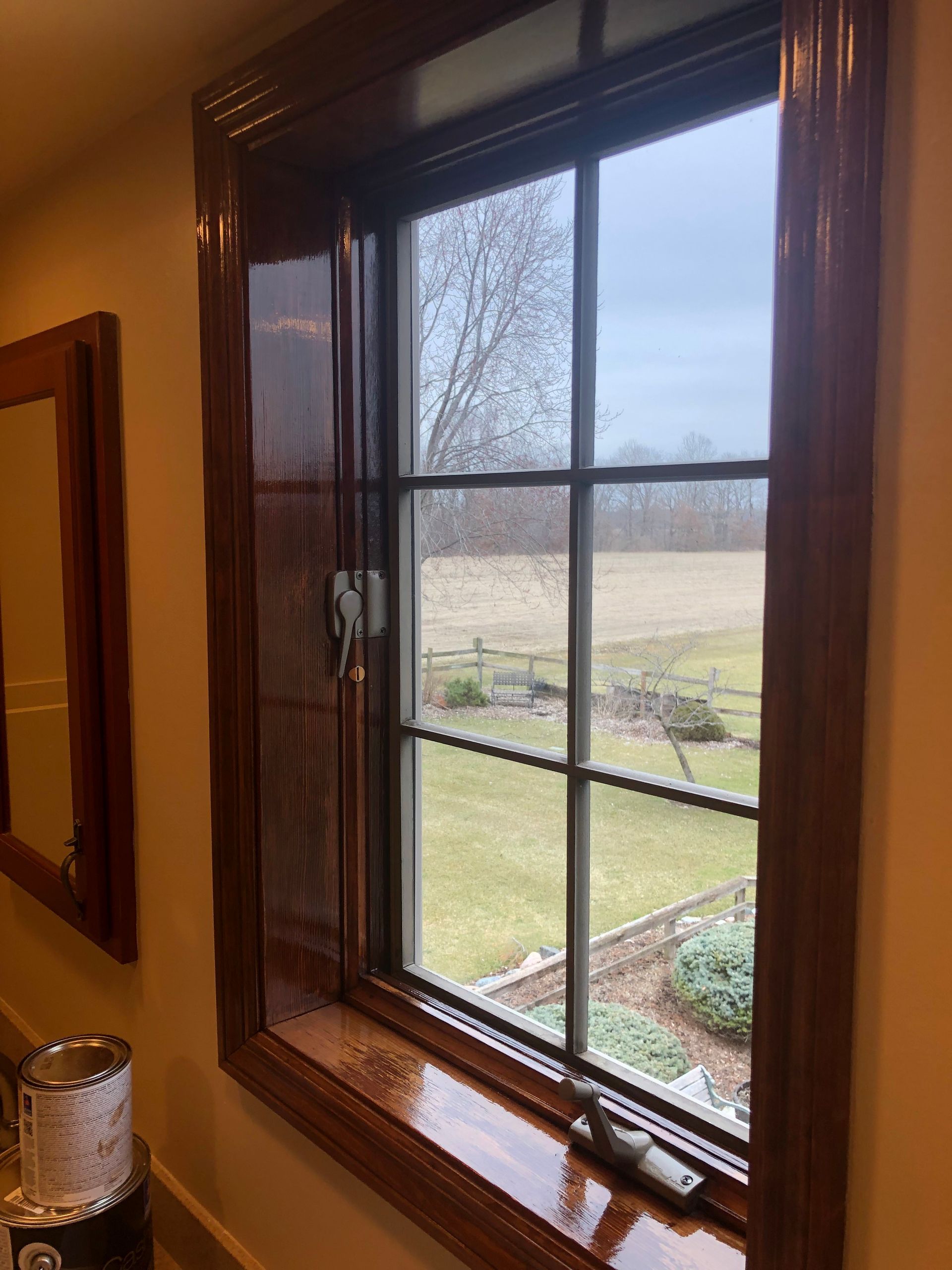 Wood-framed window with a view of a grassy yard and overcast landscape outside