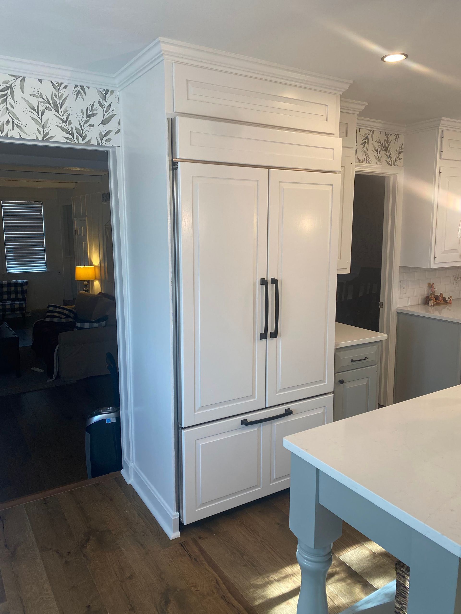 Bright white kitchen with a large built-in refrigerator, wood floor, and island counter in the foreground.