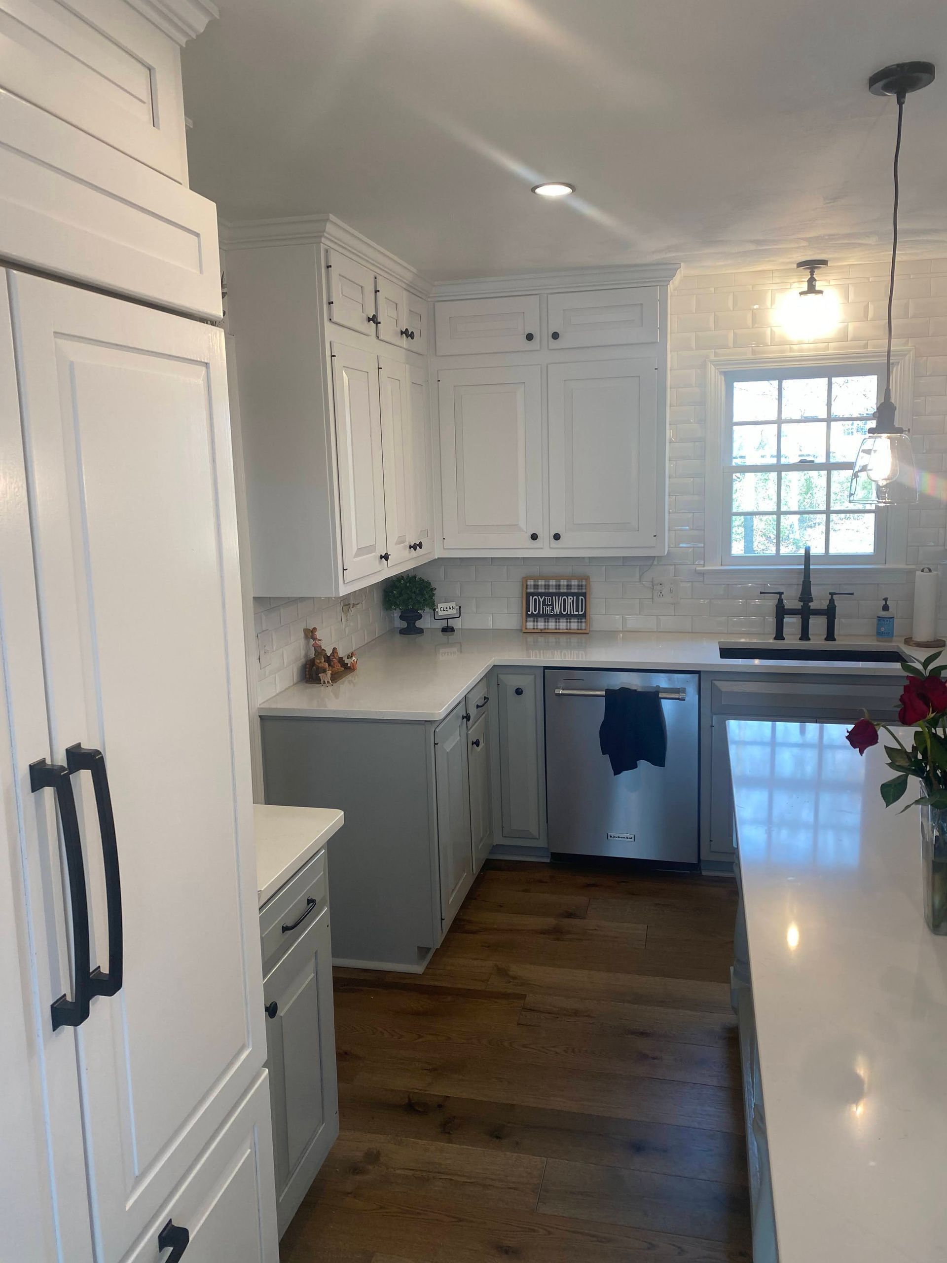 Bright white kitchen with dark wood floors, white cabinets, and a window over the sink.