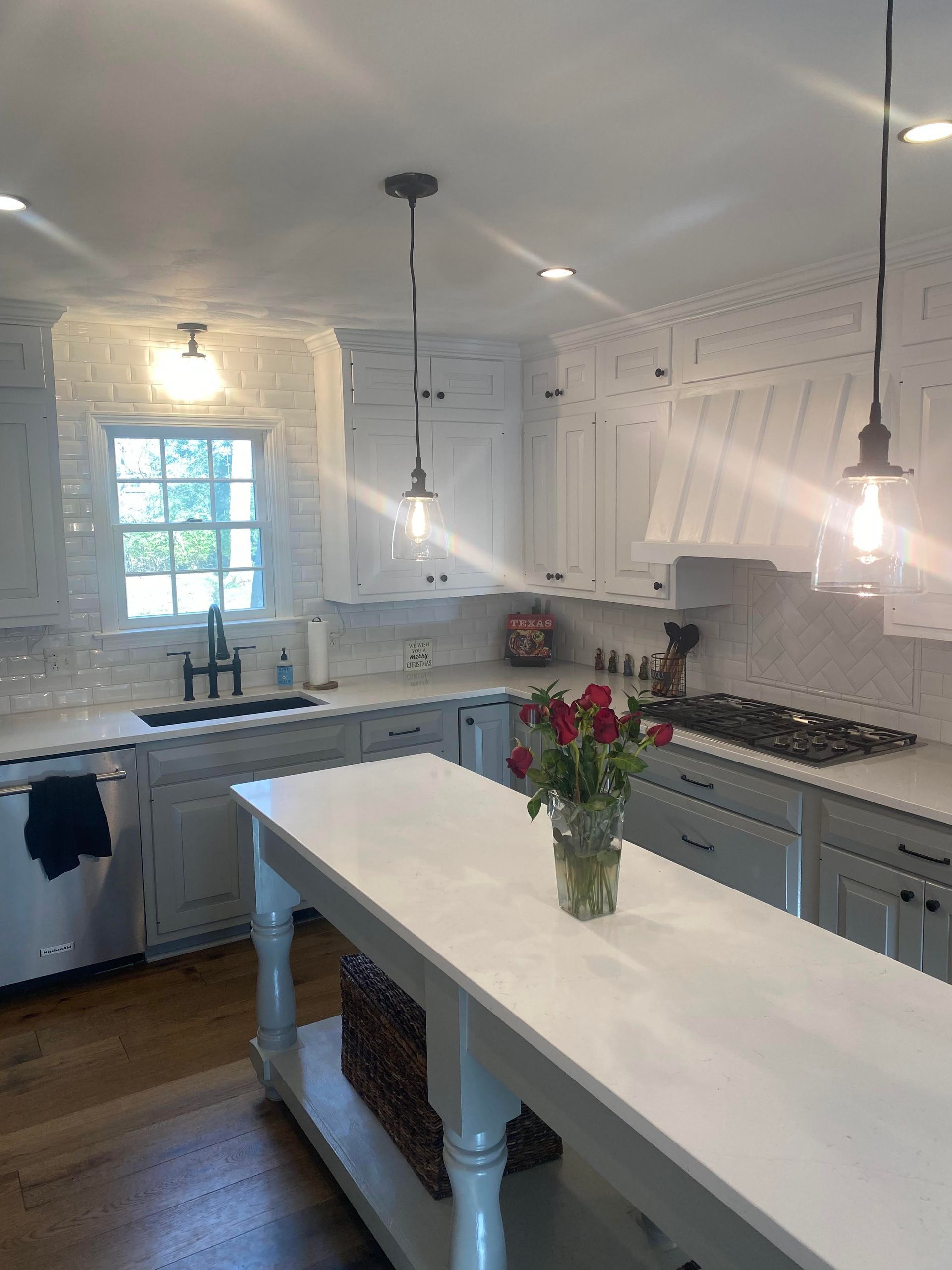 Bright white farmhouse kitchen with island, pendant lights, and a vase of red flowers on the counter