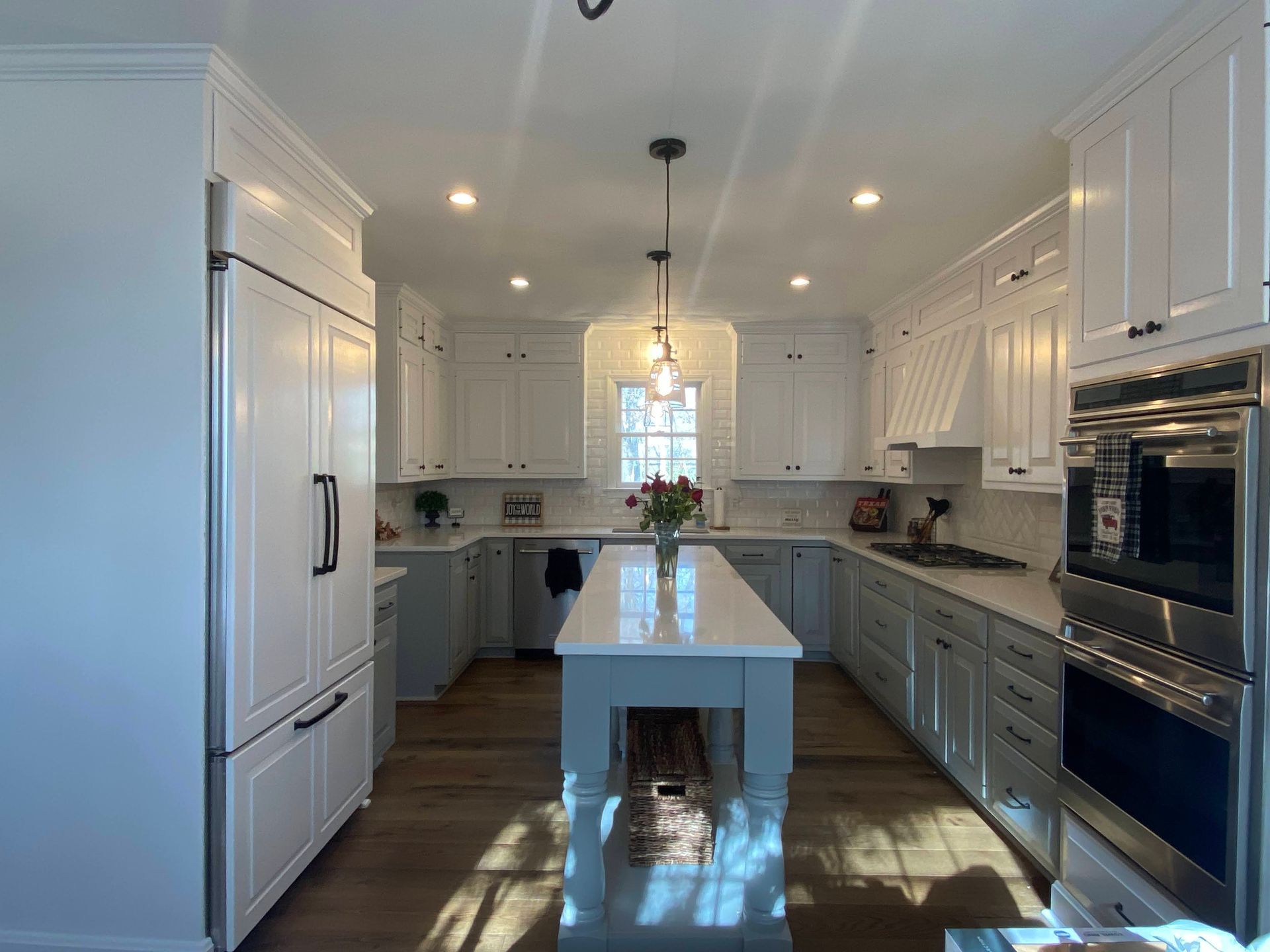 Bright white kitchen with a central island, stainless appliances, and pendant lights over hardwood floors.