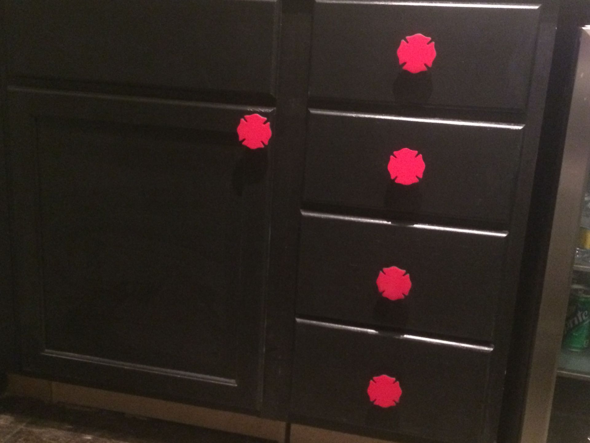 Dark cabinet with one door and four drawers, each marked by a red circular sticker.