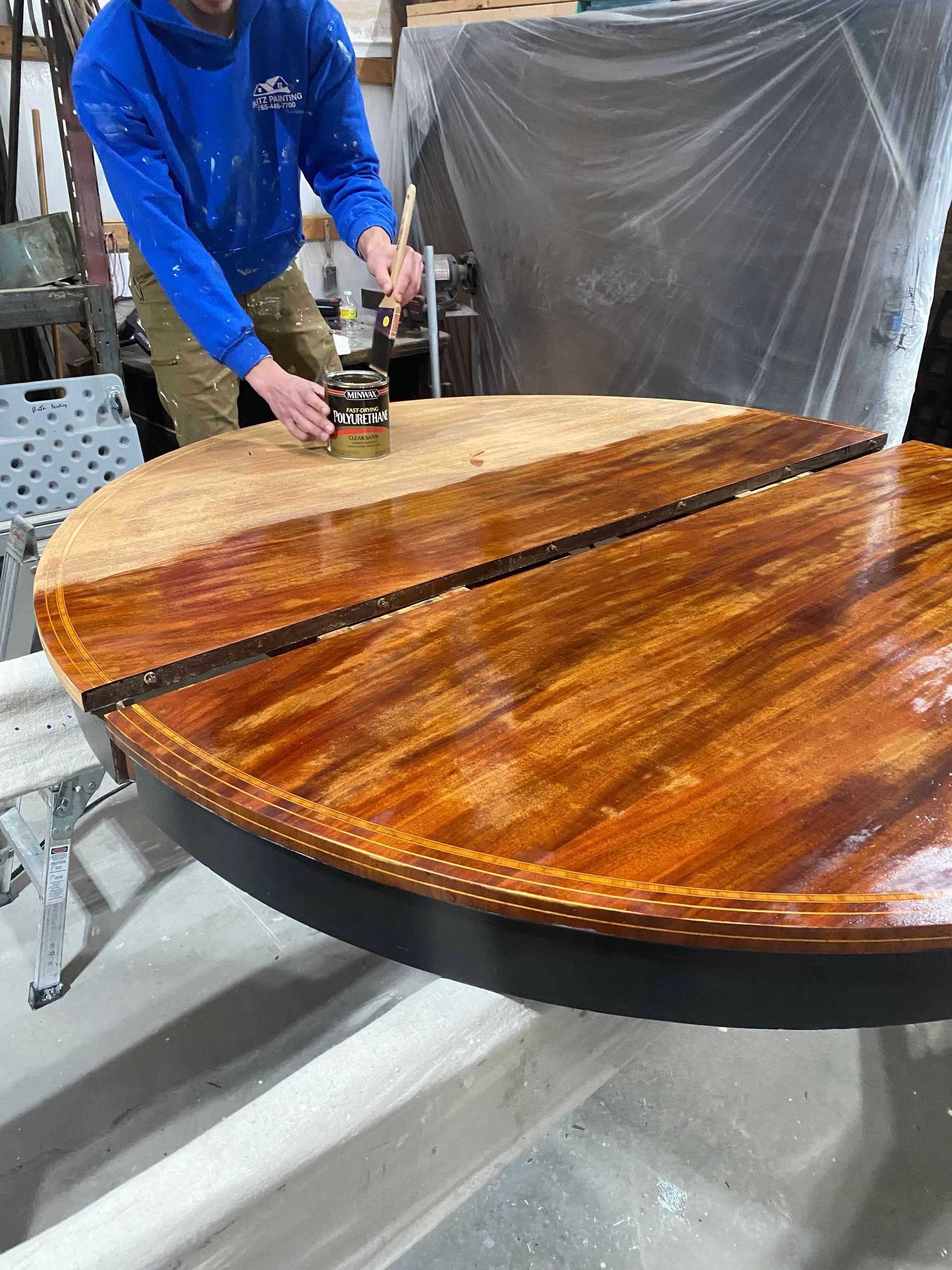 Worker sanding a round wooden table top in a workshop