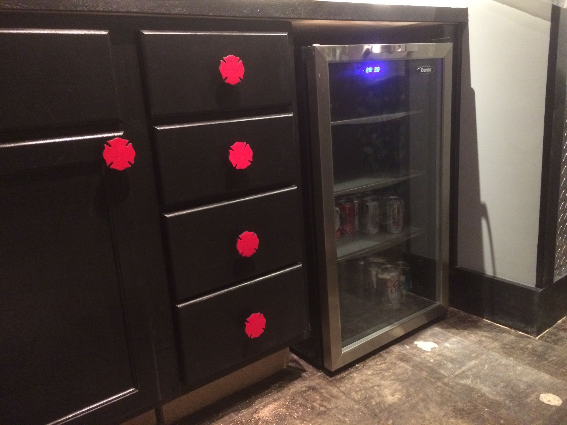 Dark kitchen cabinets beside a small glass-door beverage fridge on a tiled floor.