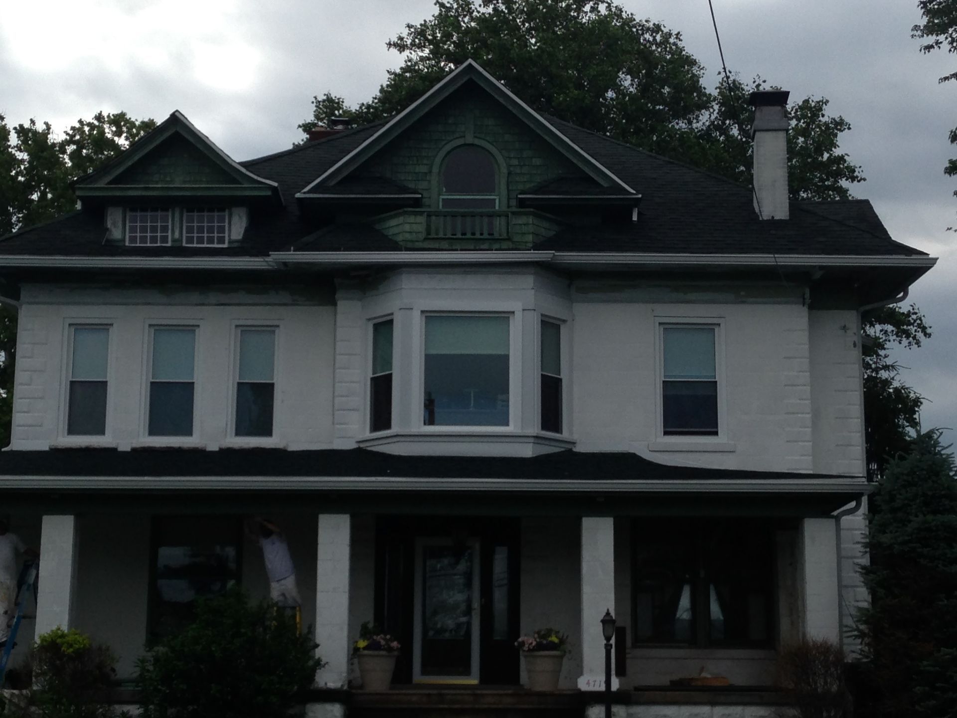 Large white two-story house with dark roof and porch under cloudy skies