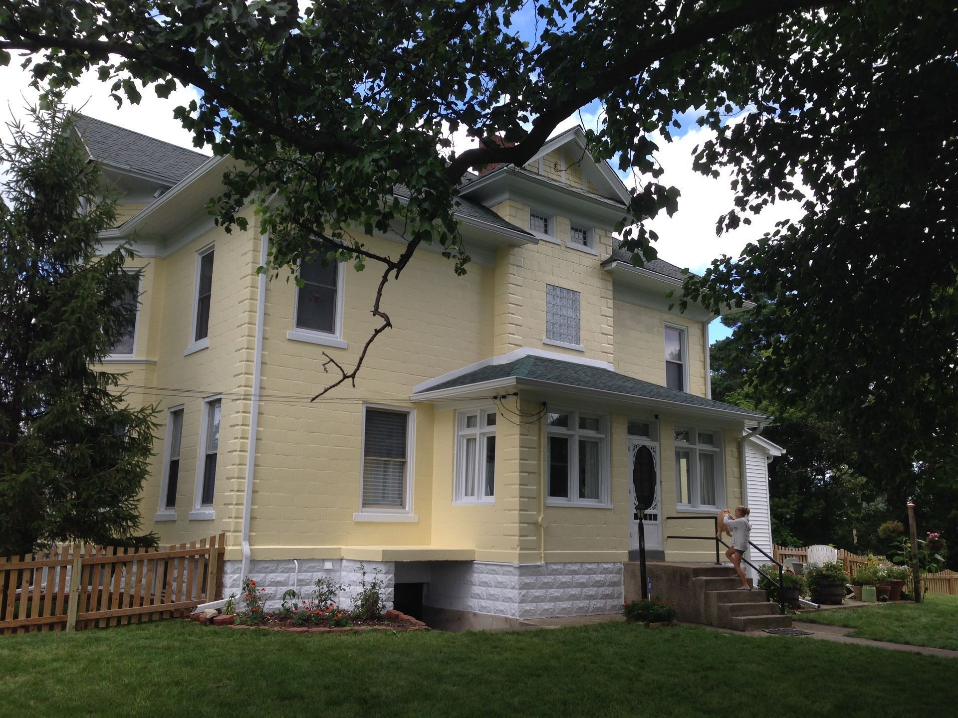 Yellow two-story house with white trim, porch, and front steps under tree branches