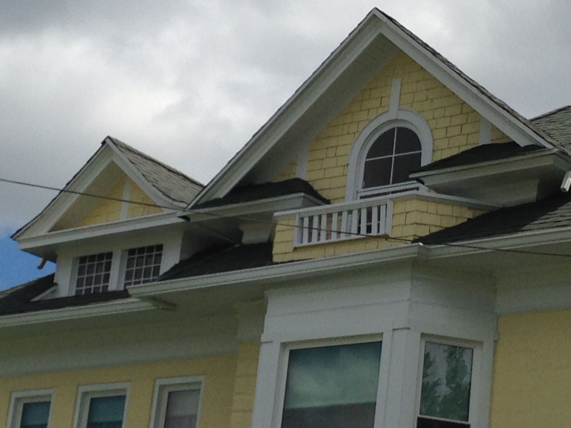Yellow house with white trim and arched attic window under a cloudy sky