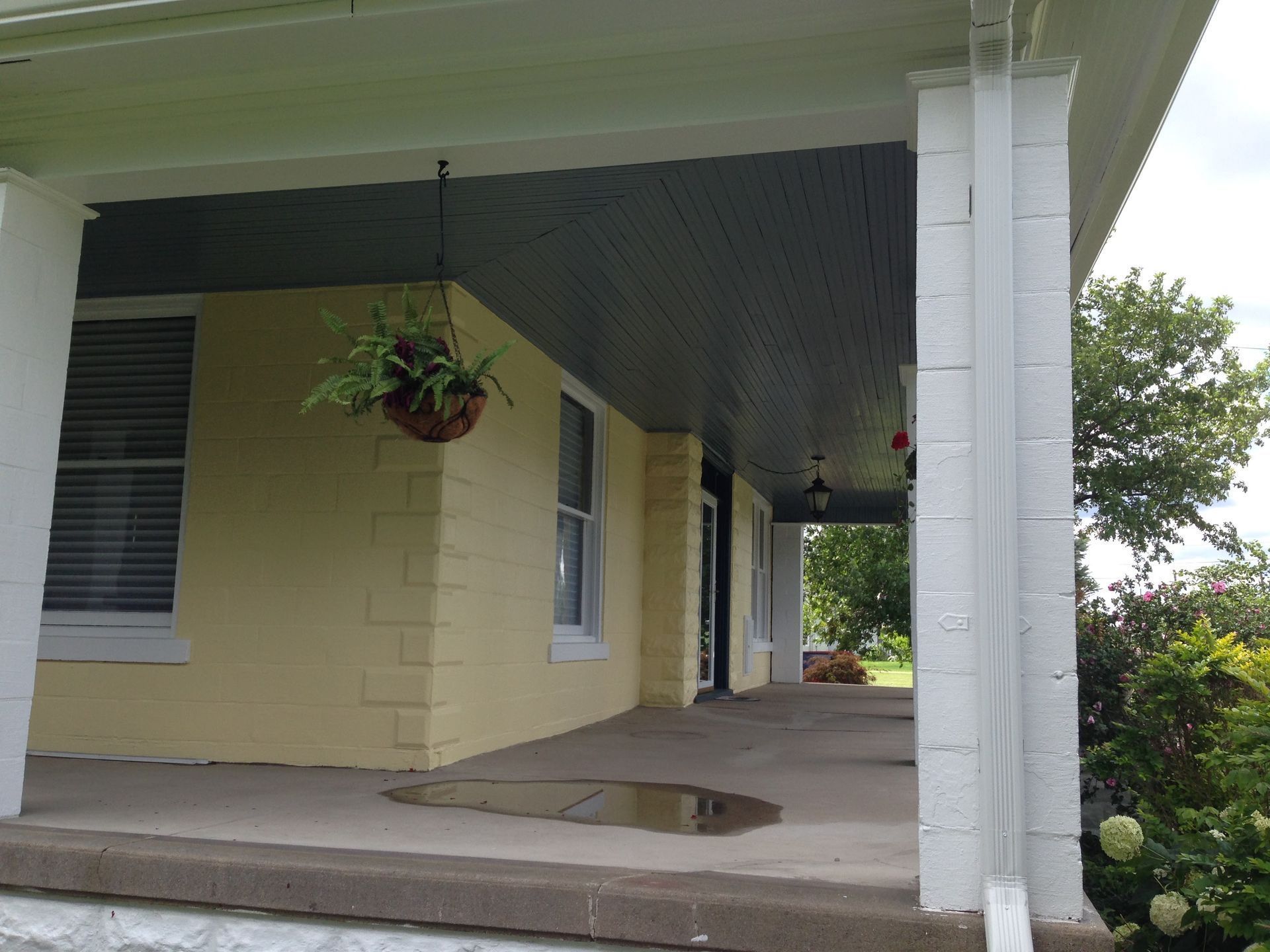 Covered porch with yellow siding, white columns, and a hanging plant at a house entrance.