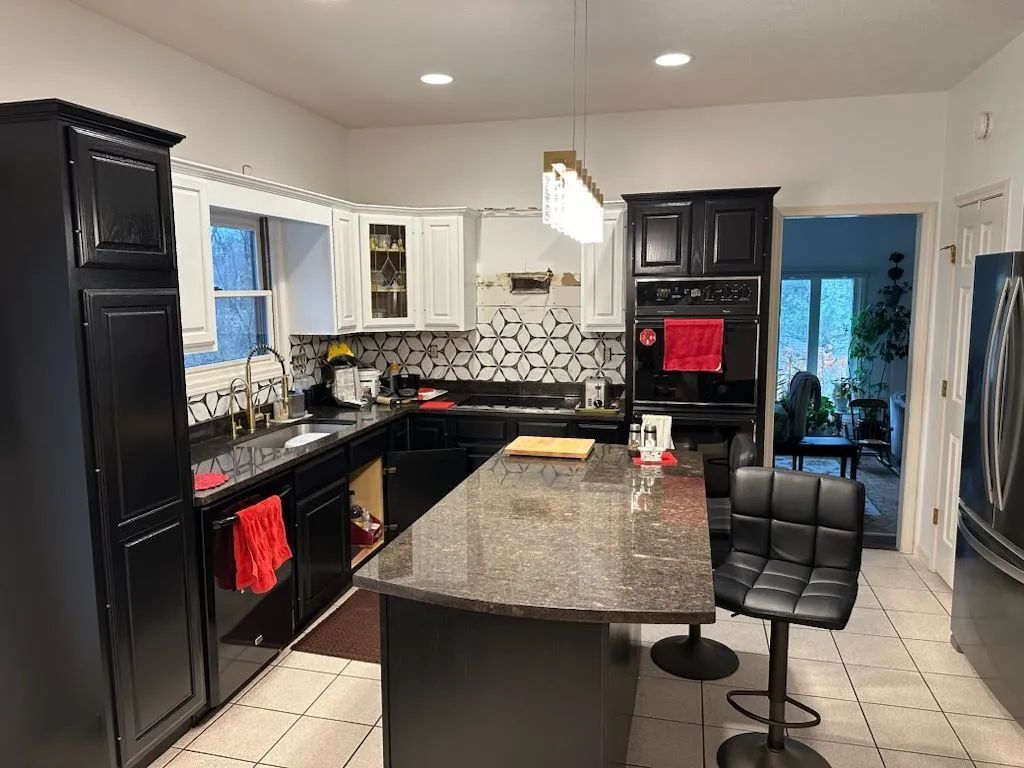 Modern kitchen with black cabinets, granite island, tiled floor, and a bar stool near the counter.