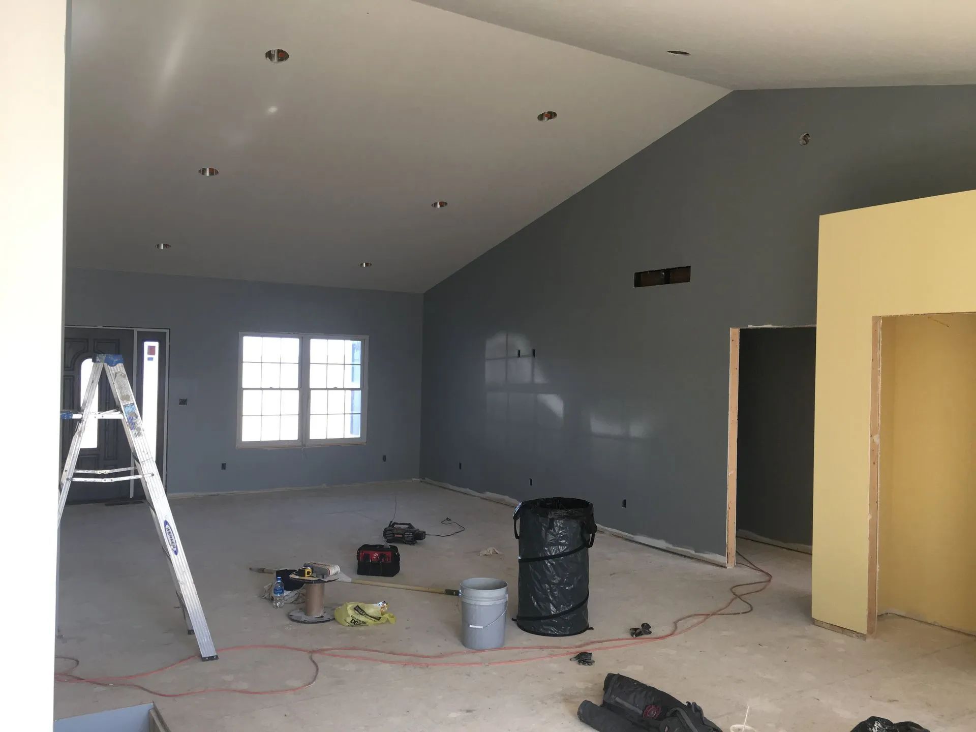 Empty room under renovation with ladder, tools, and gray walls under a vaulted ceiling