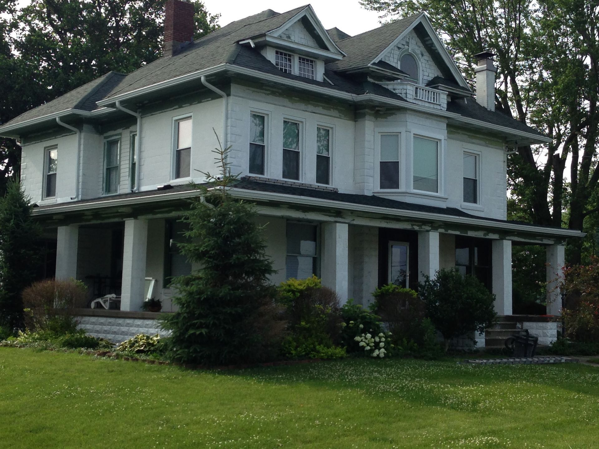 Two-story white Victorian house with green roof and wraparound porch on a grassy lawn