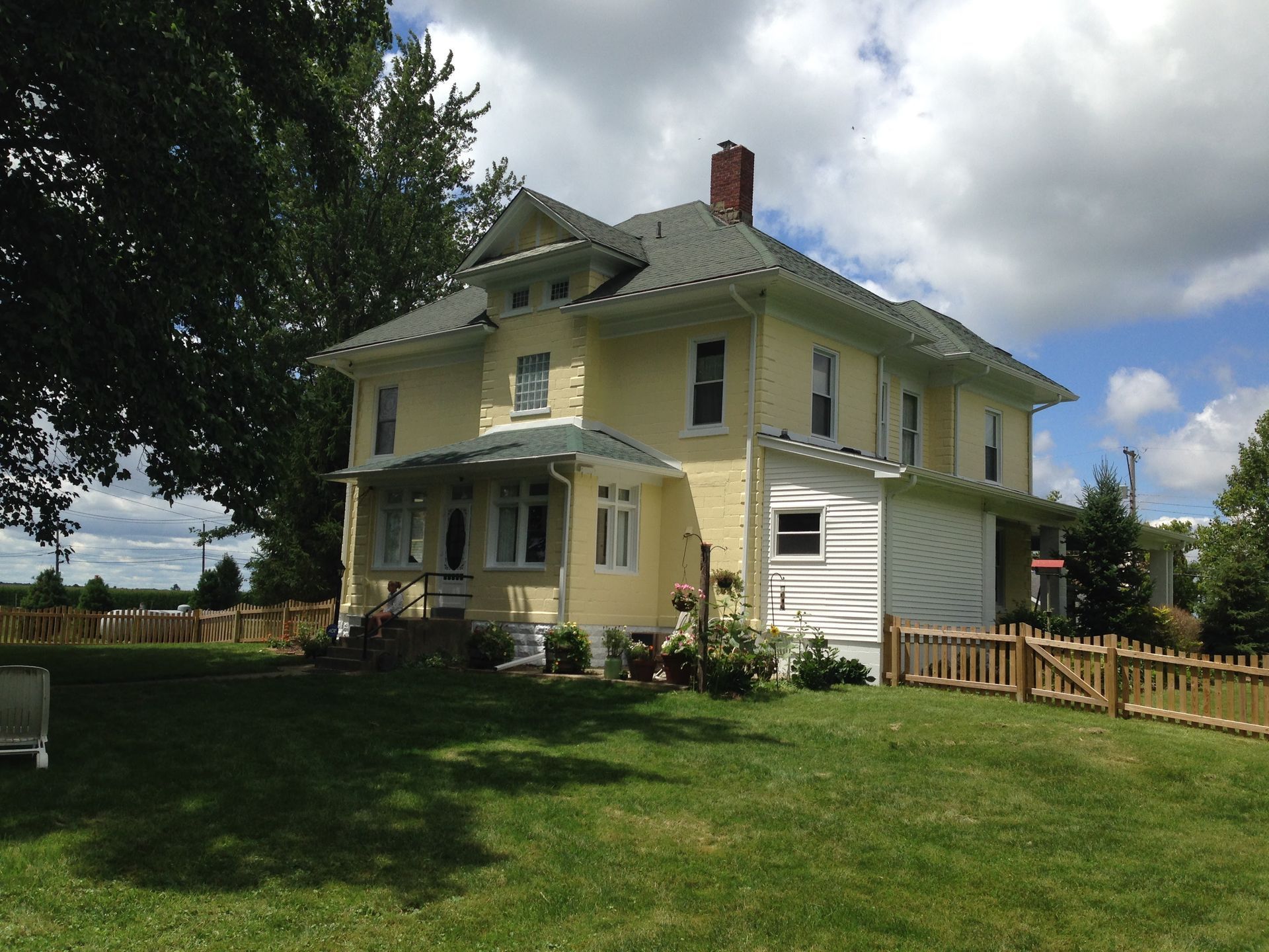 Yellow two-story house with white trim and porch on a grassy lawn under cloudy skies