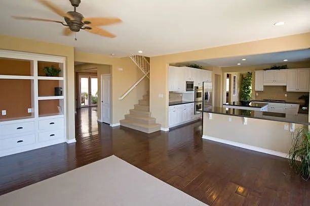 Bright open-concept living room and kitchen with dark wood floors, beige walls, staircase, and ceiling fan