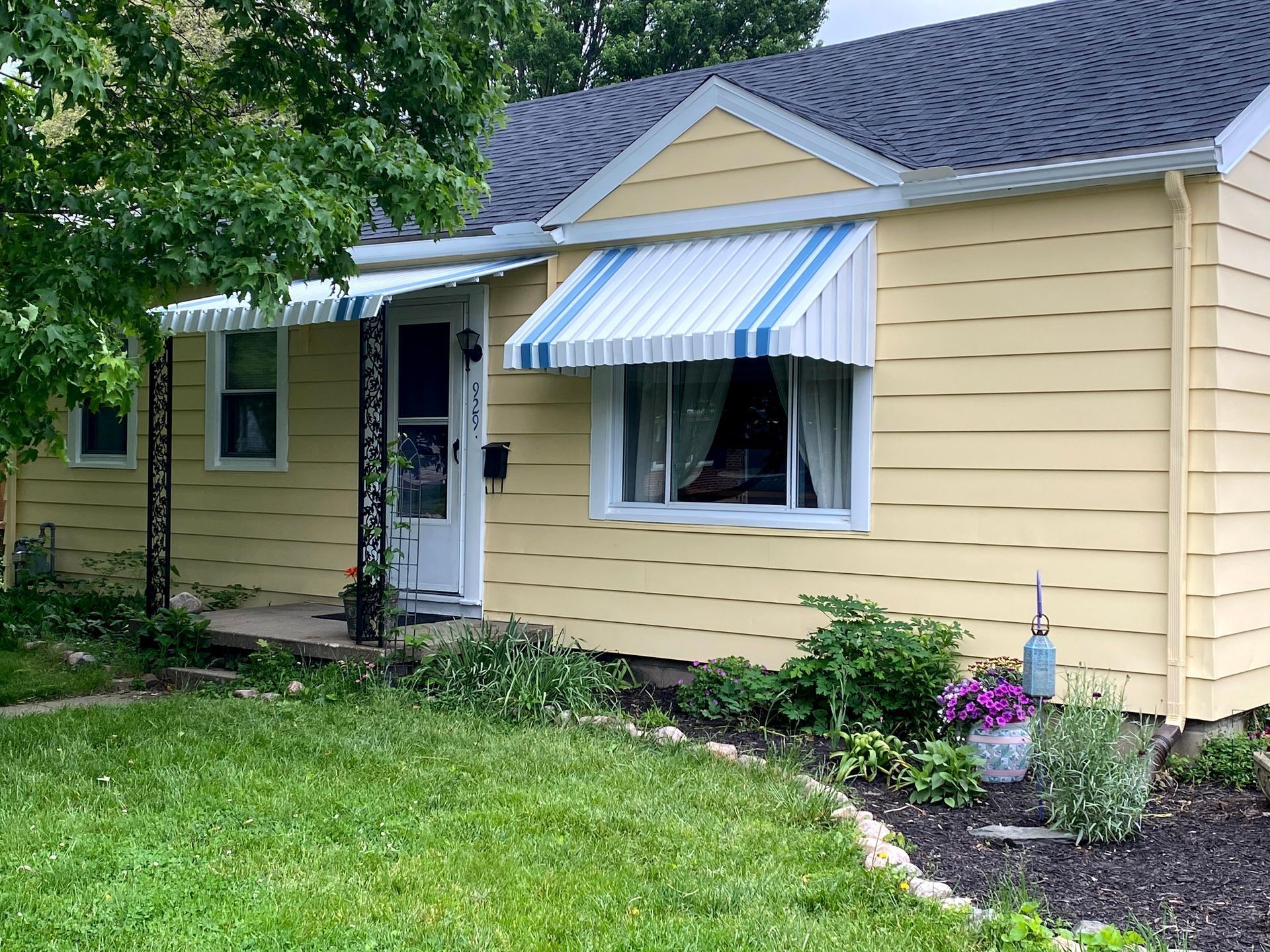Yellow house exterior with blue-and-white striped awnings and a small front garden