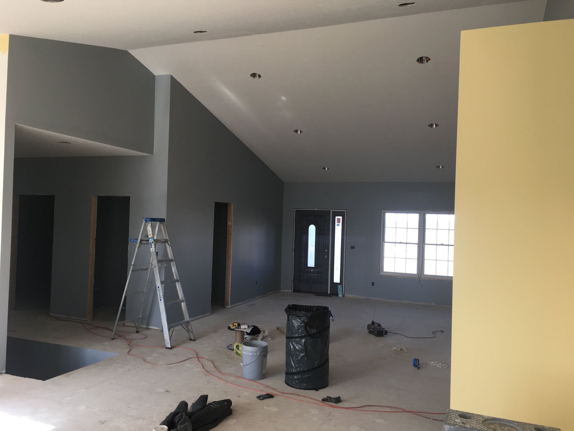 Unfinished interior with gray walls, ladder, paint cans, and construction debris on the floor.