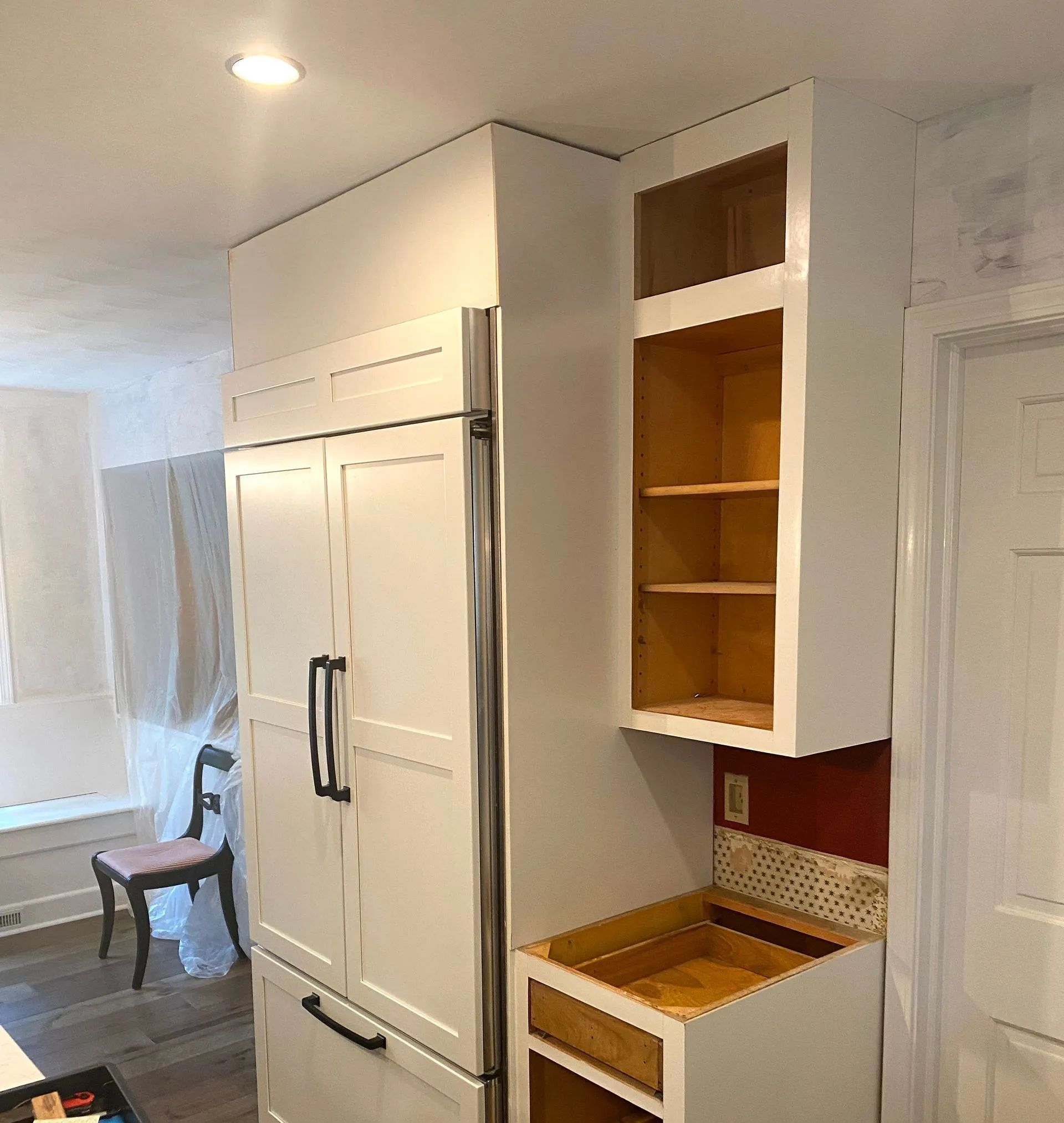White kitchen with built-in refrigerator, open cabinet, and a small counter shelf beside a doorway.