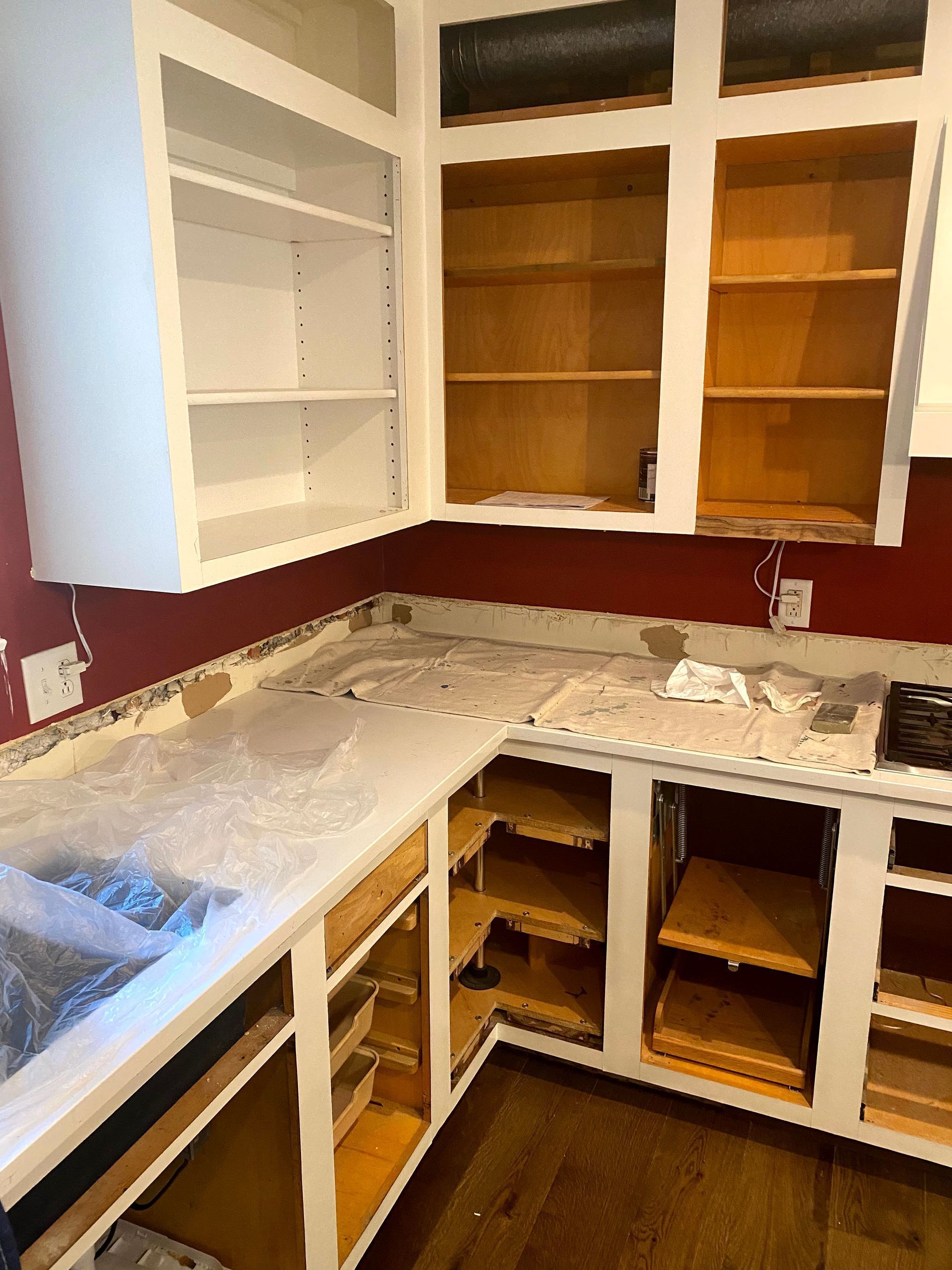 Partially renovated kitchen with white cabinets, open shelves, and countertops covered in protective plastic