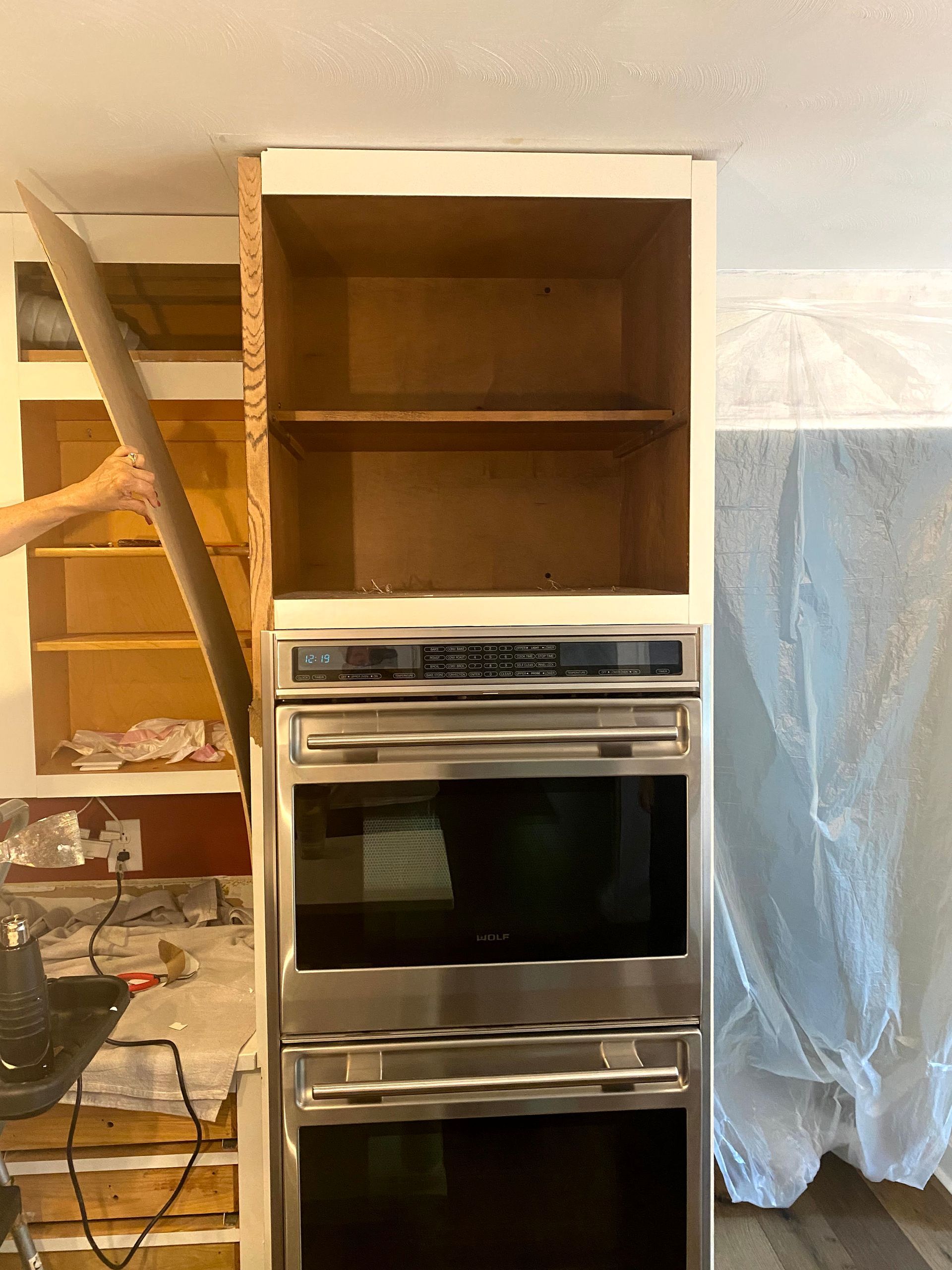 Partially installed built-in oven and cabinet unit in a room under renovation with a draped sheet nearby