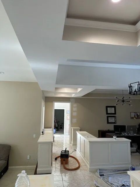 Open living room with vaulted ceiling, white trim, sofa, chandelier, and an exercise bike near a hallway