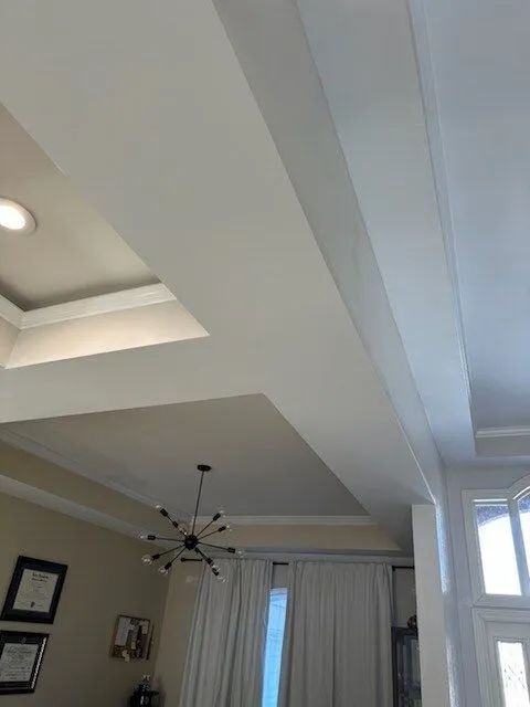 Ceiling with recessed tray design, chandelier, curtains, and skylight in a living room