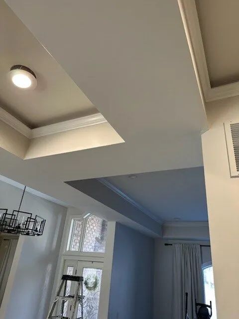Modern living room ceiling with recessed lights and skylight, showing white walls and curtains